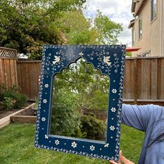 a person holding up a blue mirror with flowers on it