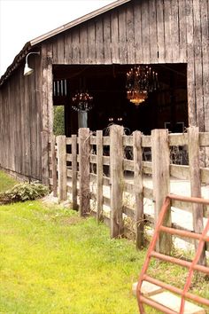 an old barn with chandeliers hanging from it's roof and wooden fence