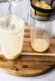 a wooden cutting board topped with a blender next to jars filled with yellow liquid