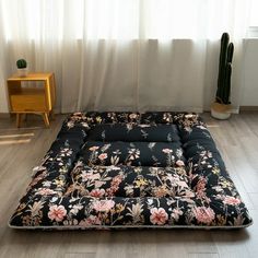 a black and pink flowered futon mattress sitting in front of a window next to a potted cactus