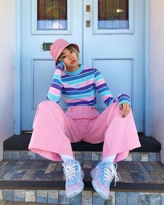 a woman sitting on the steps in front of a blue door wearing pink pants and a striped shirt