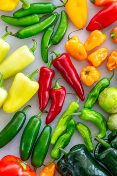 many different colored peppers on a white surface with green and red peppers in the middle