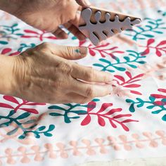 two hands are working on a piece of fabric that has been decorated with flowers and leaves