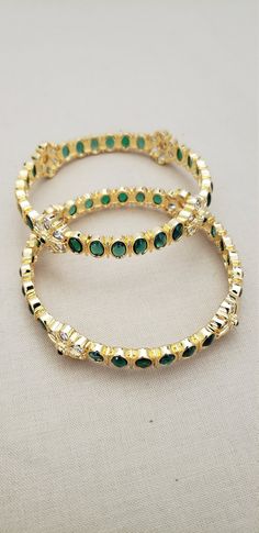 * Handcrafted Gold Plated 2 Bangle Set. * Bangles with pretty Semi Precious Emerald and CZ stones * High Quality 22 K Gold Plated bangles * Sold as a set of 2. Gorgeous gold-plated bangle/ bracelet best exemplifies the careful craftsmanship done on it -- a specialty at Nemali Jewelry. It has special tone of elegance attached to it. The intricate handmade design of the bangle / bracelet set gives it a fresh and original look. Look your best with this elegant-looking bangle / bracelet set from the Green Bangles Set, Emerald Bangles, Green Bangles, Kundan Bangles, Glass Bangles, Bangles Set, Gold Plated Bangles, Bangle Bracelet Set, Bangles Indian