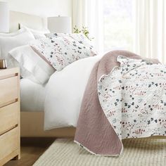 a bed with white and pink comforters in a bedroom next to a window,