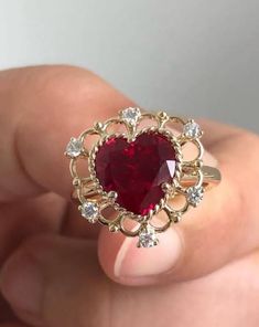 a heart shaped ruby and diamond ring in someone's hand with white diamonds around it