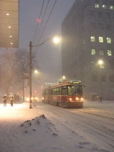 a bus driving down a snow covered street next to tall buildings and people walking on the sidewalk