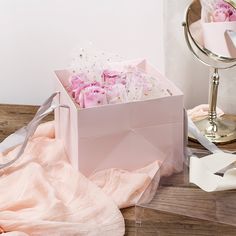 a pink box with flowers in it sitting on a wooden table next to a mirror