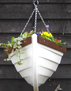 a white boat shaped planter hanging from a chain with flowers in the bottom and below it