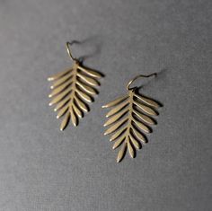 two pairs of gold earrings with leaves on them sitting on a gray surface in front of a grey background