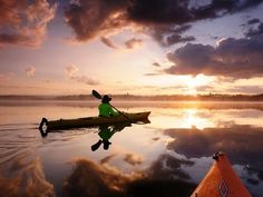 a person in a kayak paddling on the water at sunset with clouds above