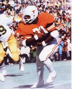 two football players running with the ball in front of an audience at a sporting event