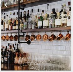 there are many bottles and glasses on the wall behind the bar counter with copper mugs