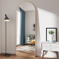 a mirror sitting on top of a wooden floor next to a white dresser and lamp