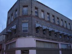 an old brick building with broken windows and shutters on the top floor is shown at dusk