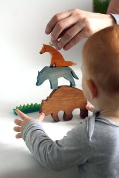 a toddler playing with wooden animals on the table in front of his mother's hand