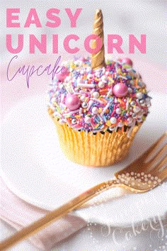 a cupcake with sprinkles and a unicorn horn on top sits on a plate next to a fork