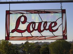 a stained glass sign that says love hanging from the side of a building with trees in the background