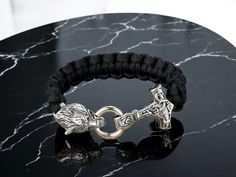 a black rope bracelet with a silver horse head clasp on top of a marble table