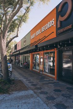 an orange and black store front with people walking down the sidewalk in front of it