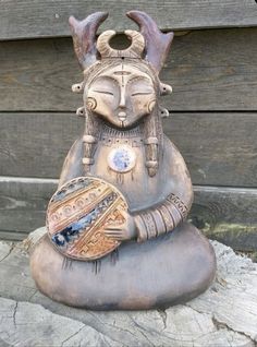 a statue of a woman with horns on her head is sitting on top of a rock