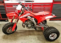 a red dirt bike parked in a garage next to some toolboxes and tools