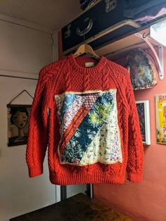 an orange sweater hanging on a rack in front of a wall with pictures and other items