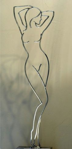 a metal sculpture of a woman standing on top of a wooden table next to a white wall