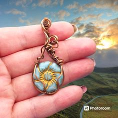 a hand holding a small pendant with a sun on it's face in front of a sunset