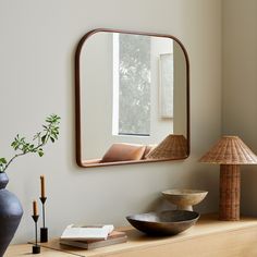 a mirror sitting on top of a wooden dresser next to a lamp and vases