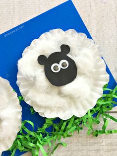 two sheep made out of paper plates sitting on top of green grass next to a blue book