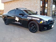 a state trooper police car parked in front of a brick building with the word state trooper on it's side