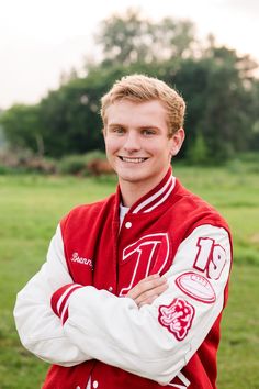 a young man in a red and white varsity jacket smiling at the camera with his arms crossed