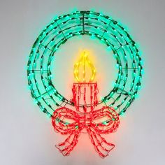 a lighted christmas wreath with a lit candle in the center on a white wall background