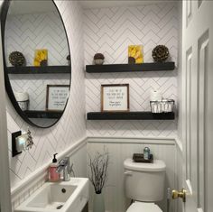 a white toilet sitting next to a bathroom sink under a round mirror on top of a wooden shelf