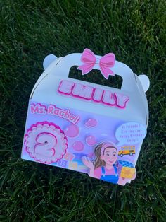 a box with a pink bow on it sitting in the grass next to a sticker