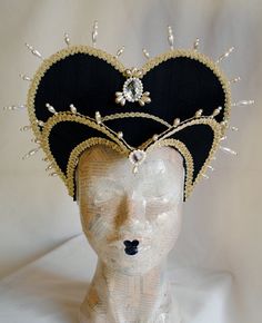 This royal Tudor inspired attifet headdress is covered with black silk shantung.It is embellished with golden cord trimming all around the edges.It is further trimmed with pearl bead details that create a halo effect. The piece is completed with clear crystal and pearl handmade elements placed at the center of both at the frond as well as the back part,to add that extra drama that we all love! The base is a headband style, completely handmade to be able to support the shape and design of the hea Elegant High Crown Headpiece For Costume, Fitted Vintage Headpiece For Carnival, Elegant Black Headpiece With Tall Crown, Vintage Black Headpieces For Costume Party, Black Structured Crown Costume Hat For Festivals, Black Costume Hats With Structured Crown For Festival, Fitted Black Halloween Headpieces, Fitted Black Headpieces For Halloween, Elegant Black Ceremonial Costume Hats And Headpieces