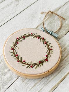 a hand embroidered christmas wreath on a white wooden surface