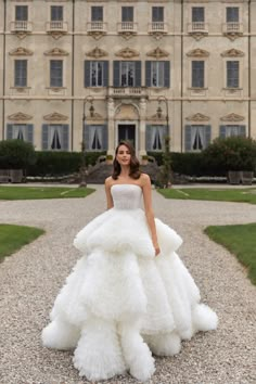 a woman standing in front of a large building wearing a wedding dress with ruffled layers