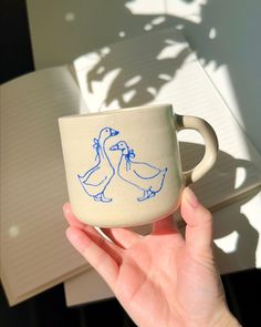 a hand holding a coffee cup with two blue birds on it and an open notebook in the background