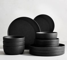 black plates and bowls stacked on top of each other in front of a white background