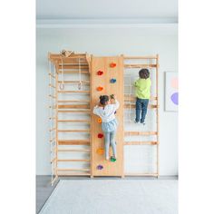 two children climbing on a climbing wall in a play room with white carpet and wooden ladders