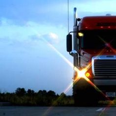 a red semi truck driving down a road at night with bright lights on the front