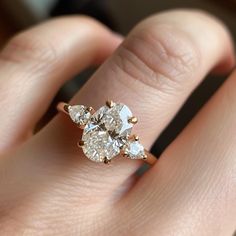 a woman's hand holding an engagement ring with three pear shaped diamonds