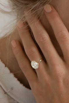 a woman's hand with a diamond ring on her left hand and the other hand holding it up to her face