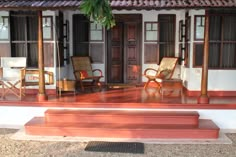 two chairs sitting on the porch of a small white house with red steps leading up to it