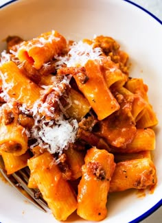 a white bowl filled with pasta covered in sauce and parmesan cheese on top