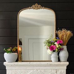 a white fireplace with vases and flowers on it in front of a black wall