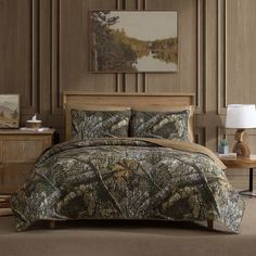 a bed with camouflage comforter and pillows in a bedroom setting that has wood paneling on the walls