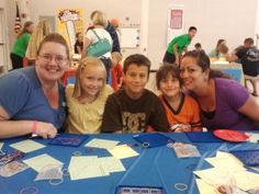 a group of children sitting at a table with paper and scissors on it, posing for the camera